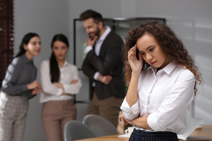 Bullying at work concept – an employee looking distressed at their desk while colleagues exhibit intimidating behaviour in the background, symbolising workplace harassment.