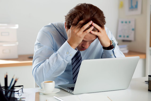 A stressed businessman holding his head in frustration while sitting at a desk with a laptop, symbolising the challenges of constructive dismissal.