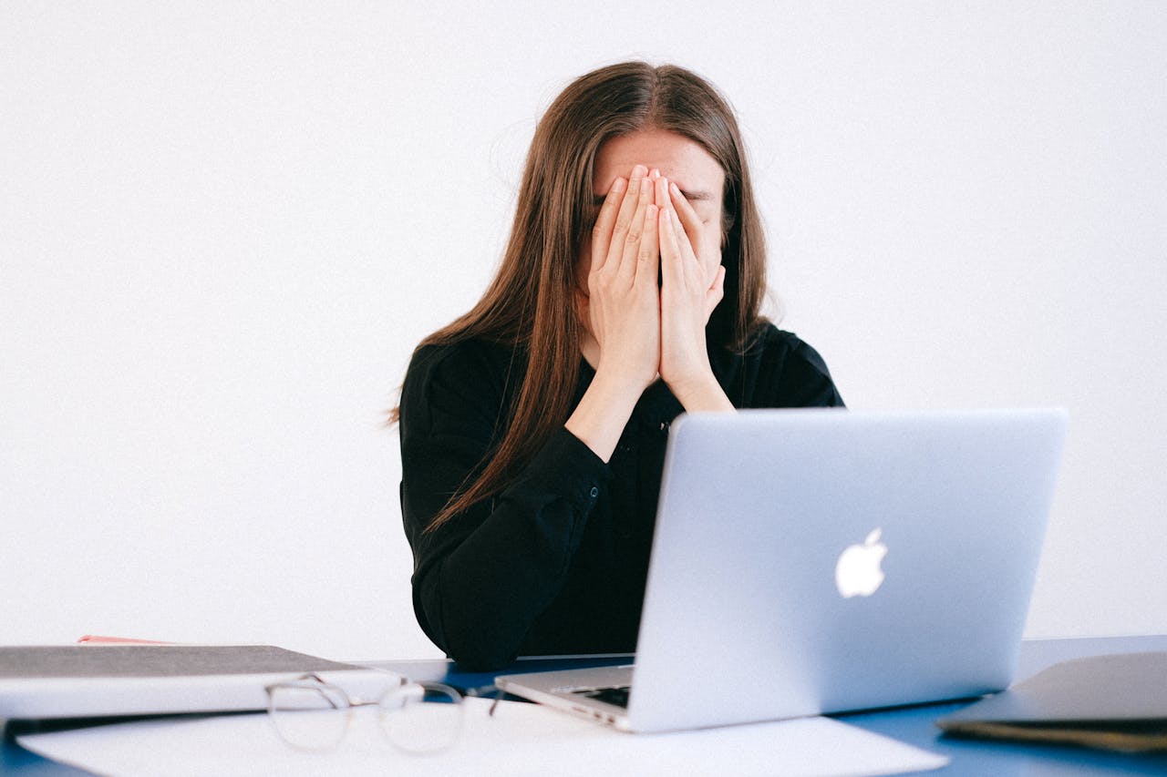 A stressed woman sitting at a desk with her head in her hands in front of a laptop, symbolising workplace difficulties and the need for legal advice on claiming constructive dismissal.