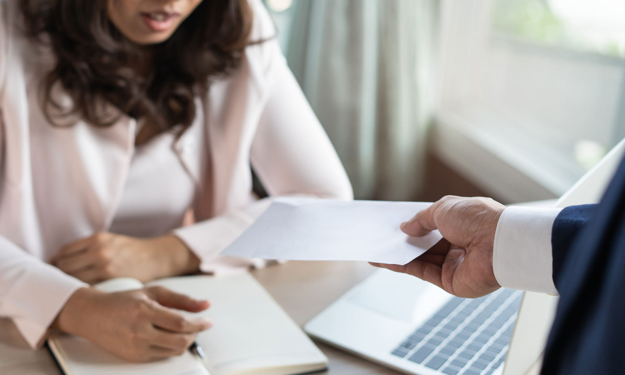 A professional handing over a document to a woman during a workplace meeting, symbolising procedural fairness in unfair dismissal claims, relevant for Locate Solicitors.