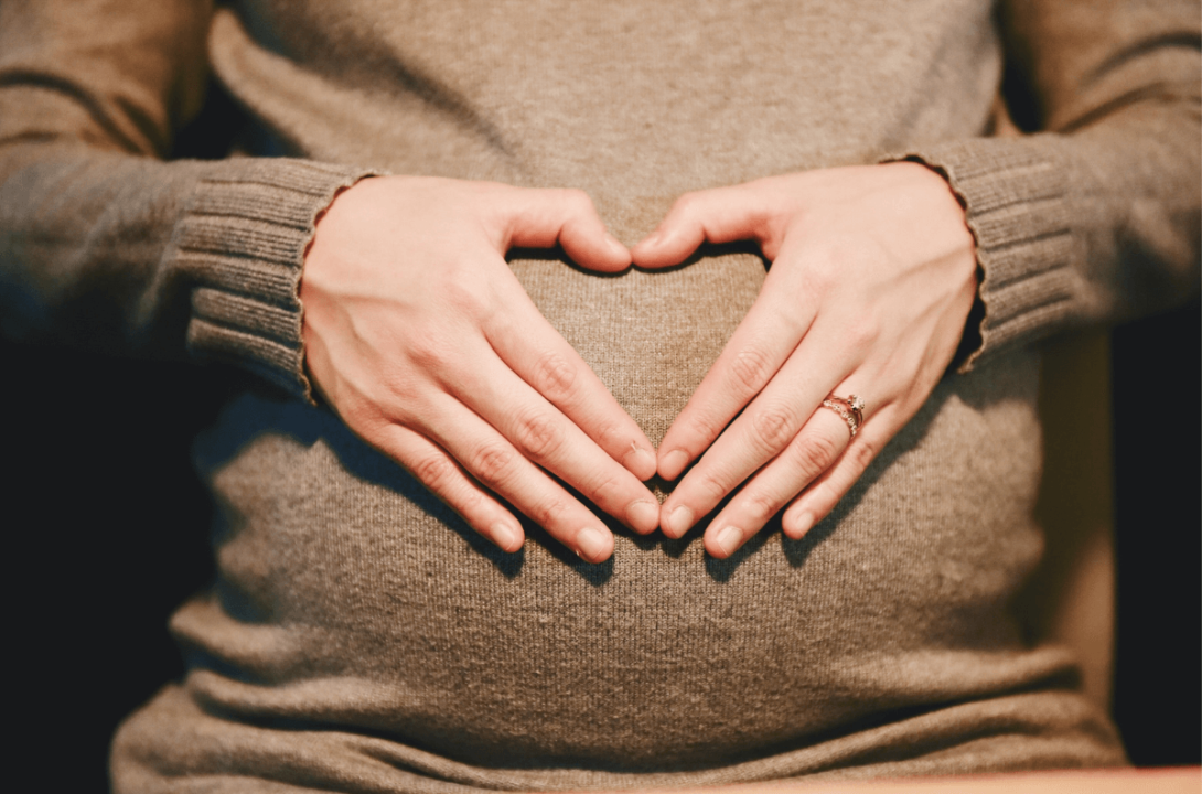Close-up of a pregnant woman forming a heart shape over her belly with her hands, symbolising maternity pay for self-employed individuals.