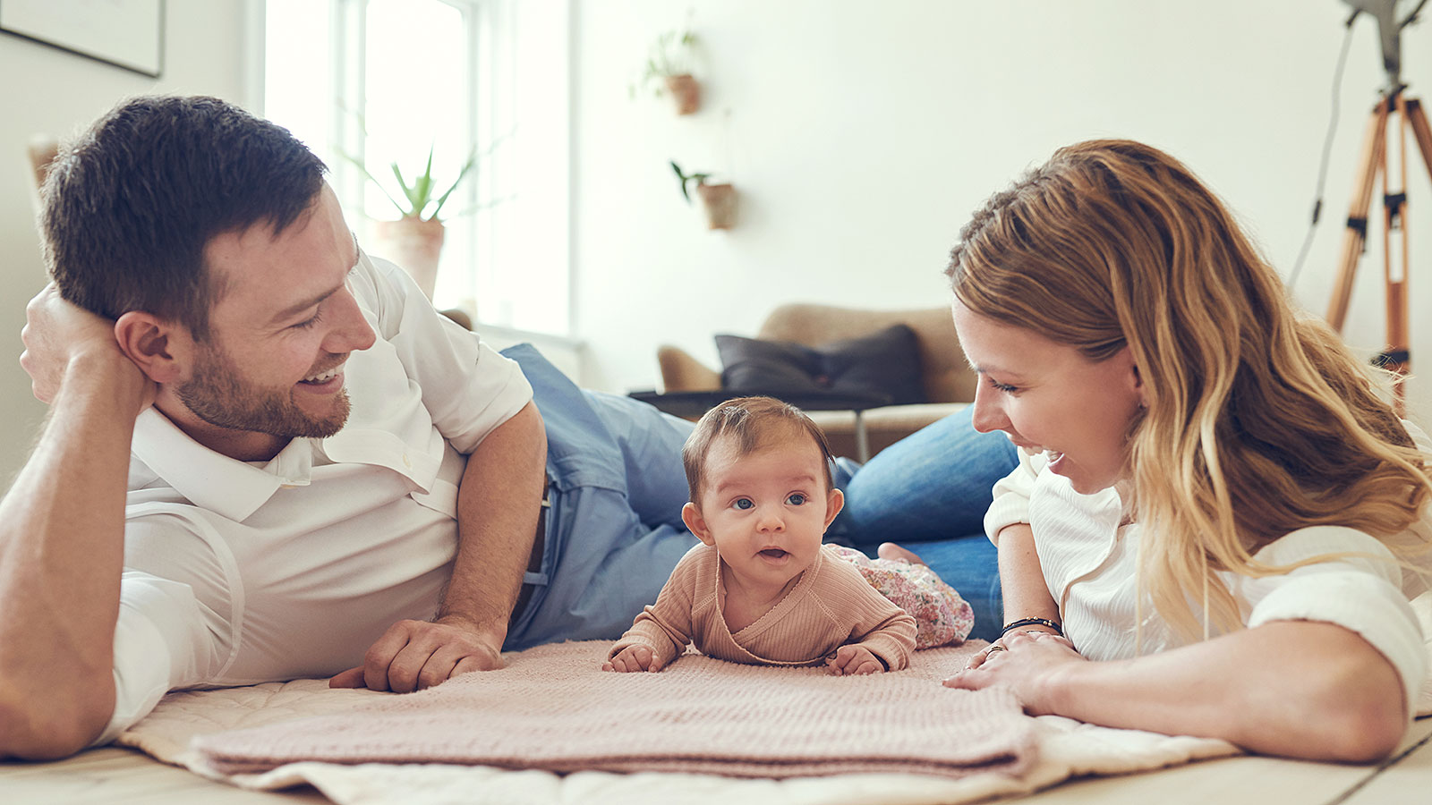 A happy family, including a mother, father, and baby, bonding on the floor at home, symbolising family life and the challenges of being pregnant during maternity leave.