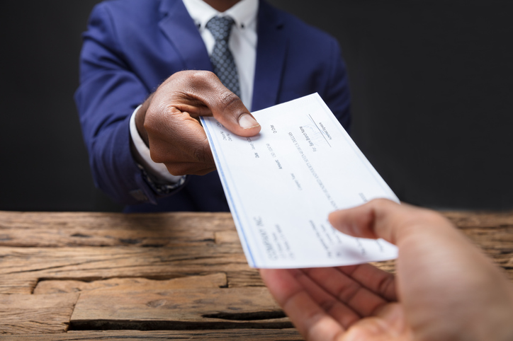 A professional in a suit hands over a cheque, symbolising the financial and legal aspects of a redundancy agreement.
