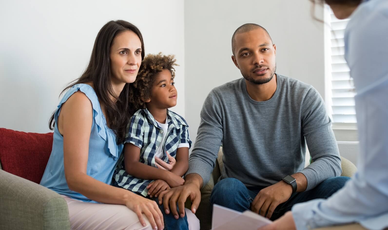 A family of three—mother, father, and child—sits together attentively during a consultation, symbolising shared parental leave and pay discussions.