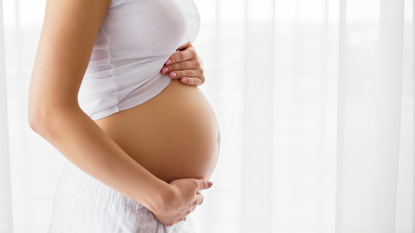 A close-up side view of a pregnant woman gently holding her baby bump, symbolising the importance of sick leave during pregnancy for health and well-being.