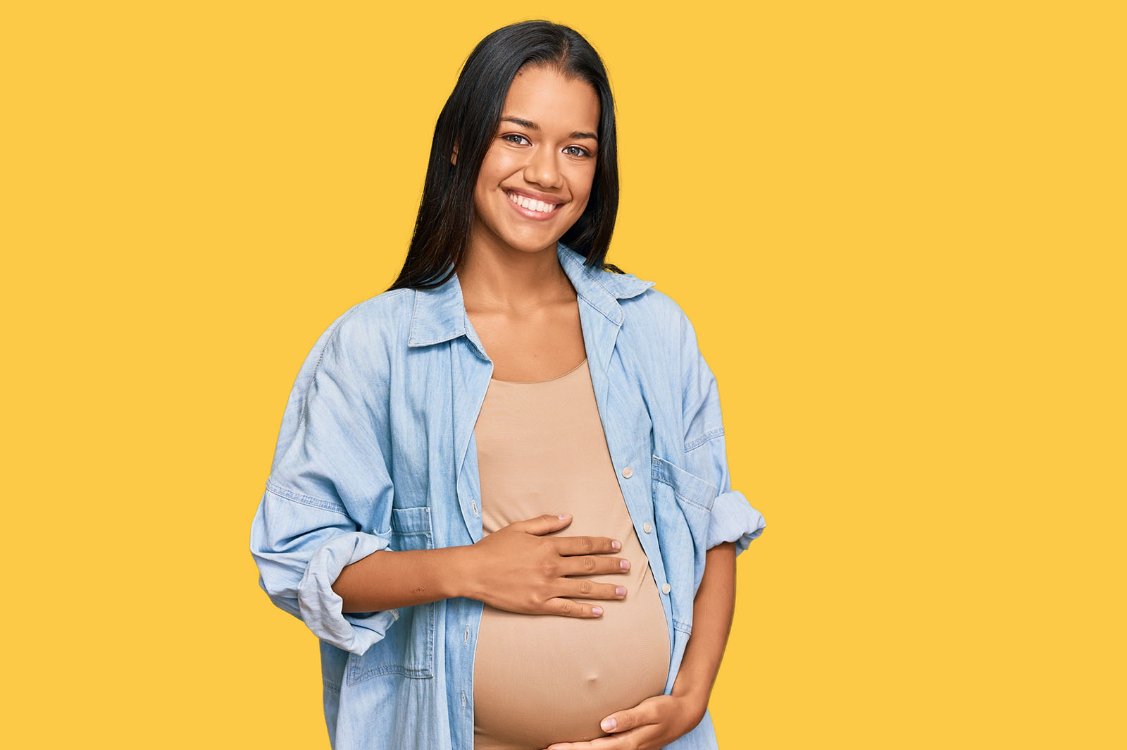 A smiling pregnant woman gently cradles her baby bump against a bright yellow background, symbolising statutory maternity pay and support during pregnancy.